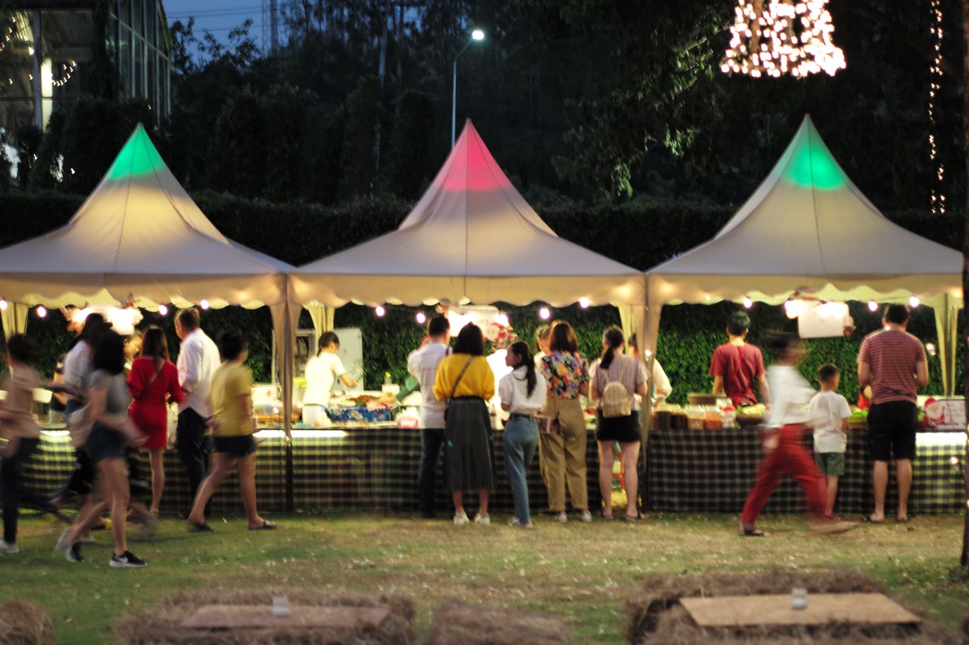 Guests queuing at lit food gazebos at an evening outdoor event