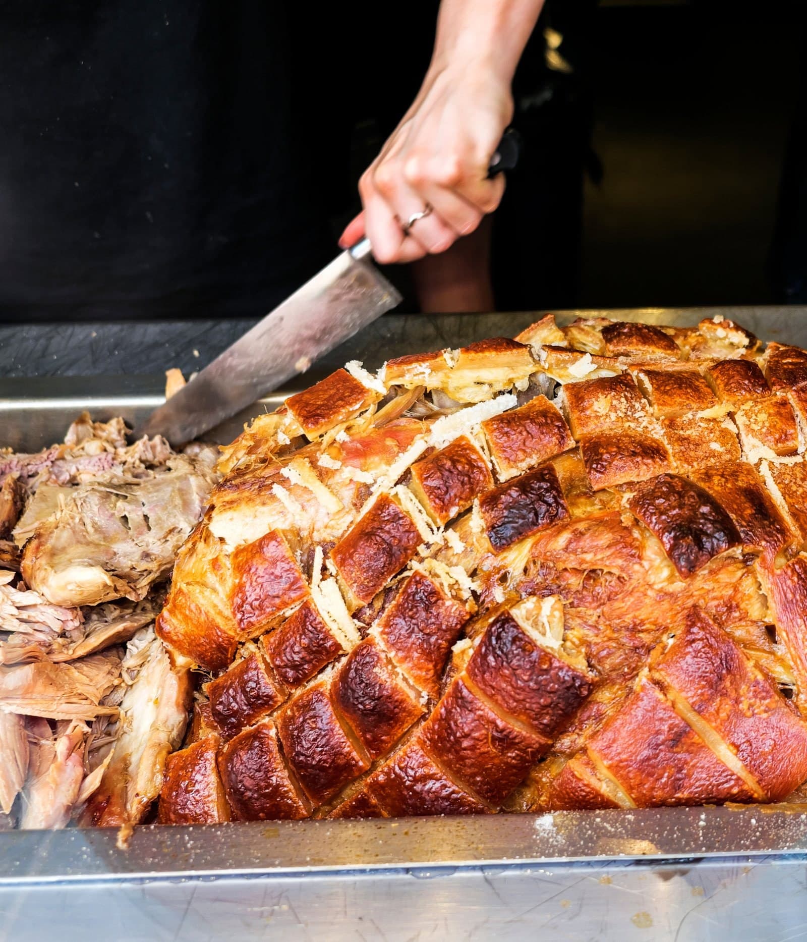 Roast hog with golden crackling being carved at the counter